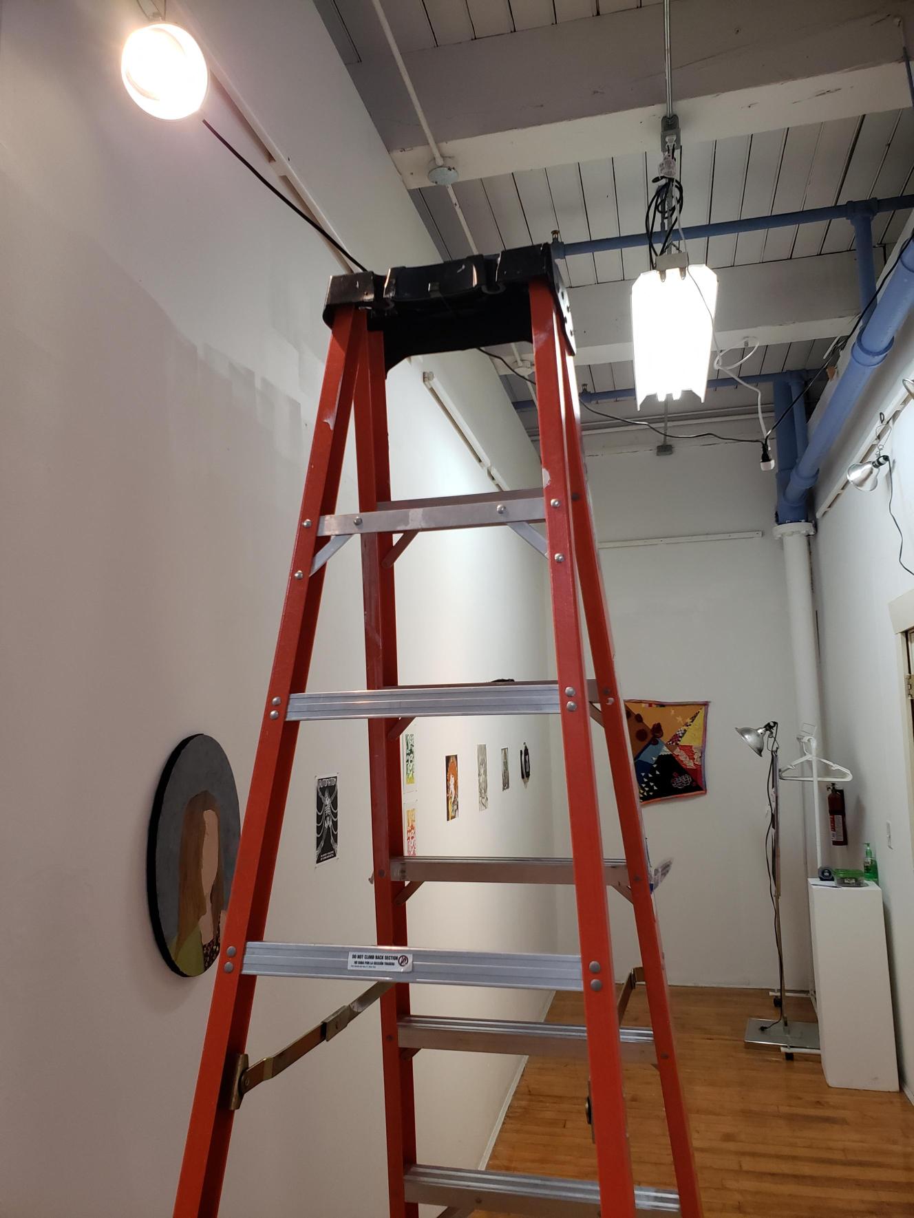 A ladder set up in the Kalamazoo College Community Studio, in front of artwork in the Department Show