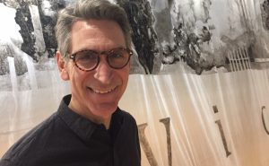 A headshot of Tom Rice in front of his artwork