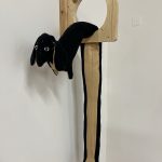 A wooden piece of toast with a hole in it; a long fabric dog is draped through the hole