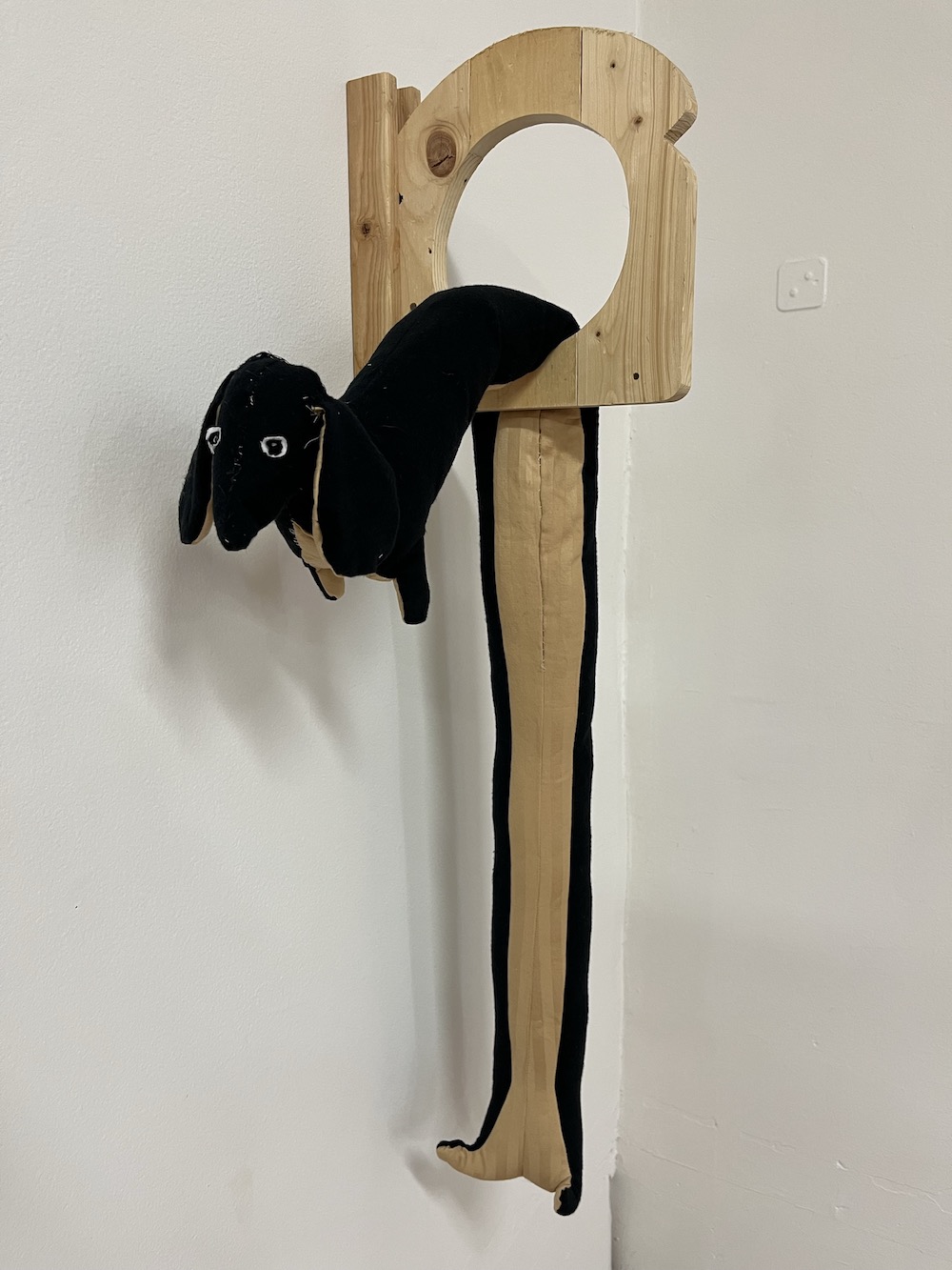 A wooden piece of toast with a hole in it; a long fabric dog is draped through the hole