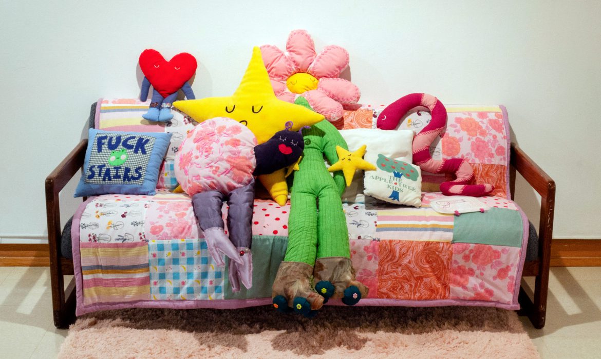 A couch with a quilt and cute, brightly colored soft sculptures on it.