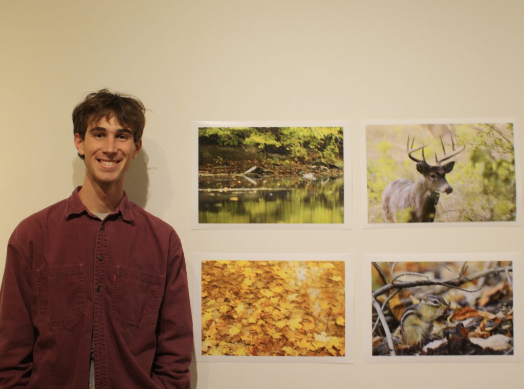 Student (Henry Black) stands next to his nature photographs