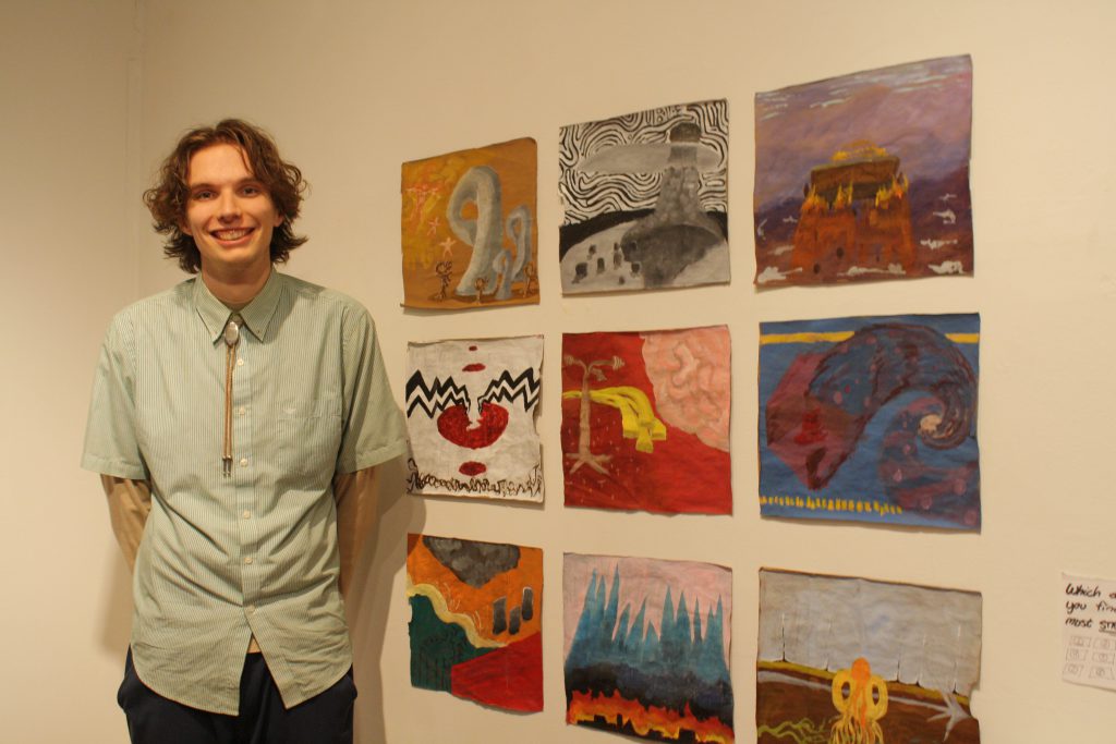 Student (Theo Niemann) stands next to his nine square paintings